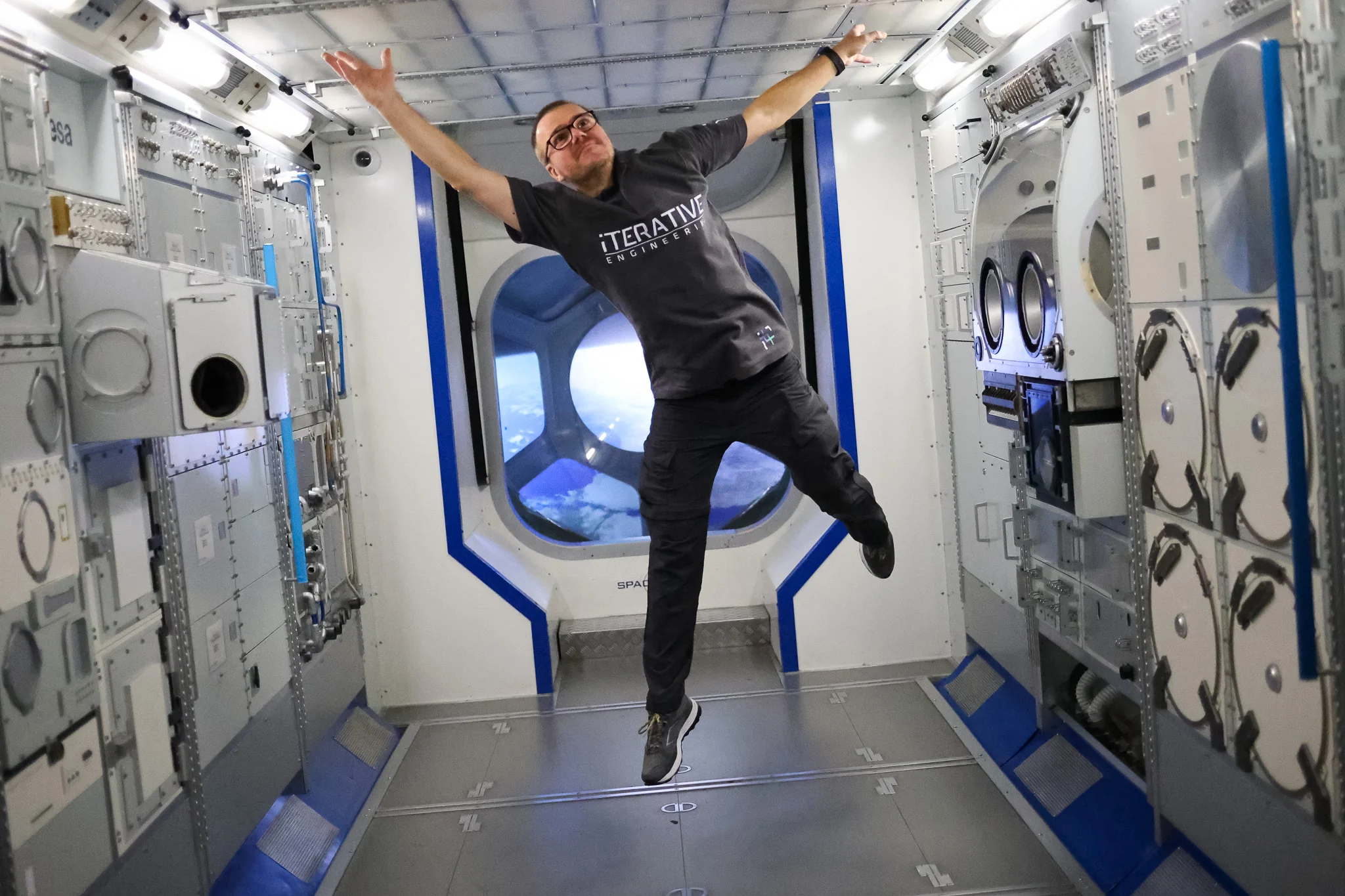 Tomasz posing with arms outstretched to imitate floating in microgravity inside an ISS module mock-up at Space Expo