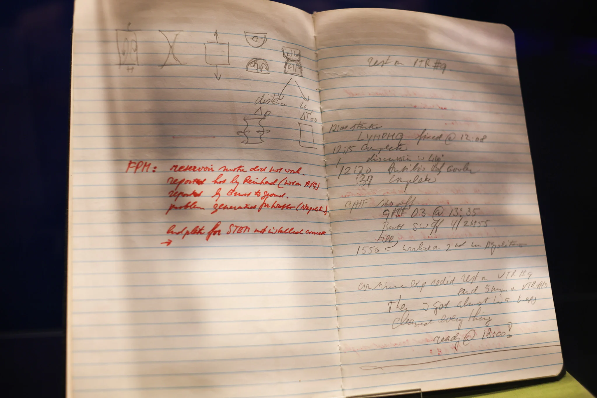Handwritten notes and sketches in an open notebook displayed in a museum case at Space Expo